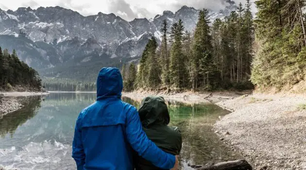 Couple in raincoats standing near body of water in mountains