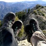 Photo of two people wearing hiking shoes and sitting on a ridge