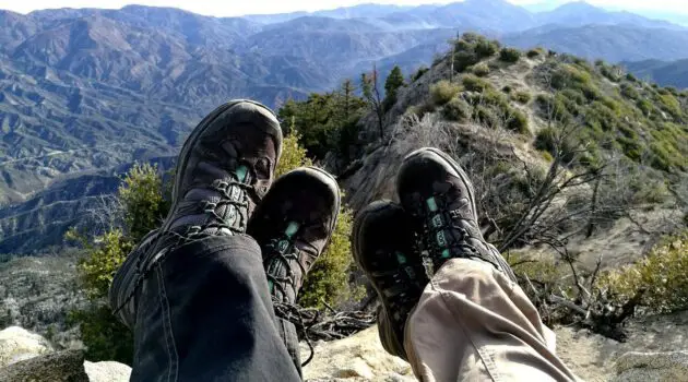 Photo of two people wearing hiking shoes and sitting on a ridge