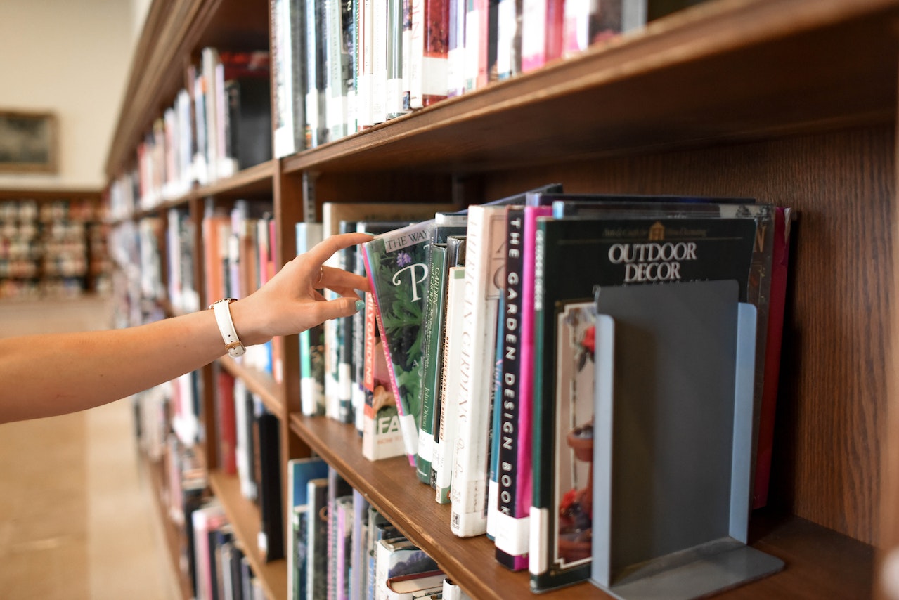 Photo of person picking out a book from a library shelf