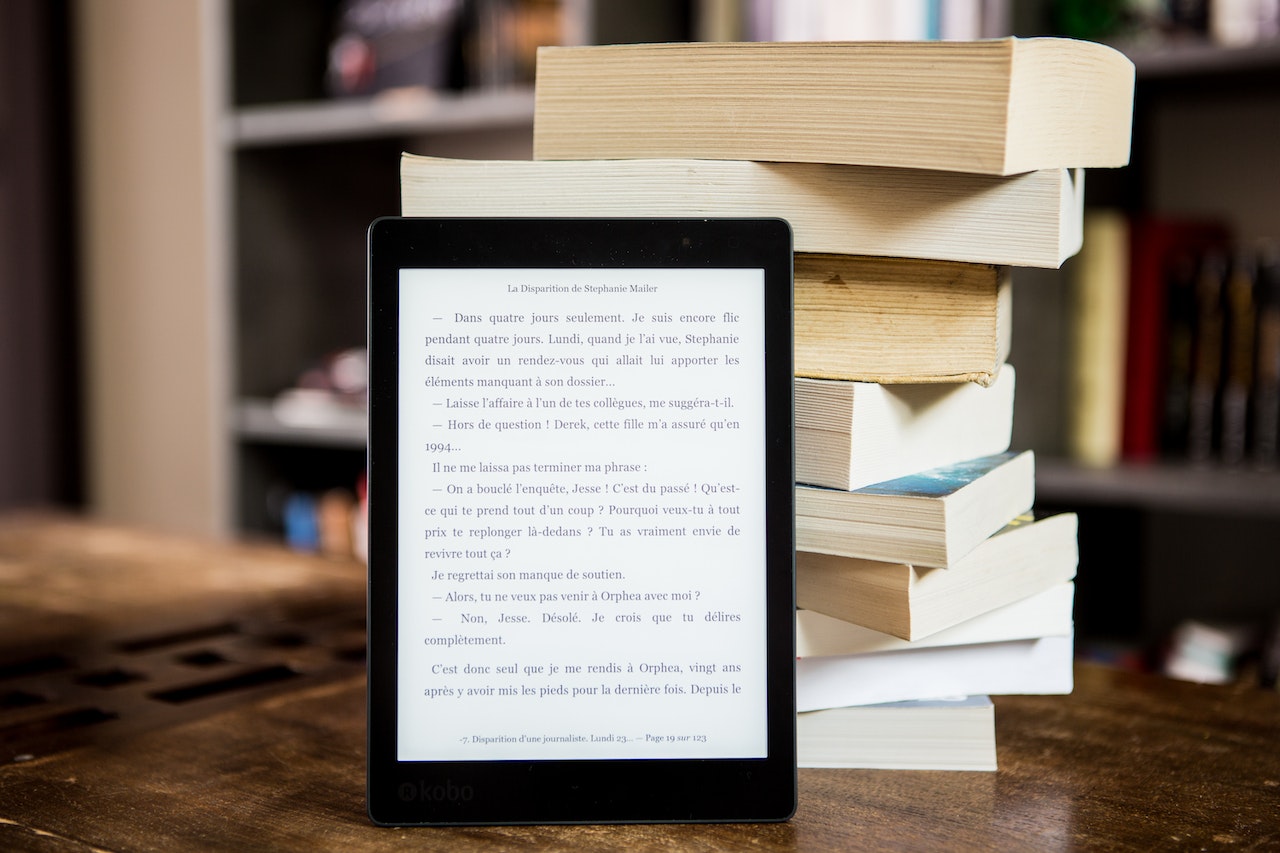 Photo of an e-reader propped up against a pile of books